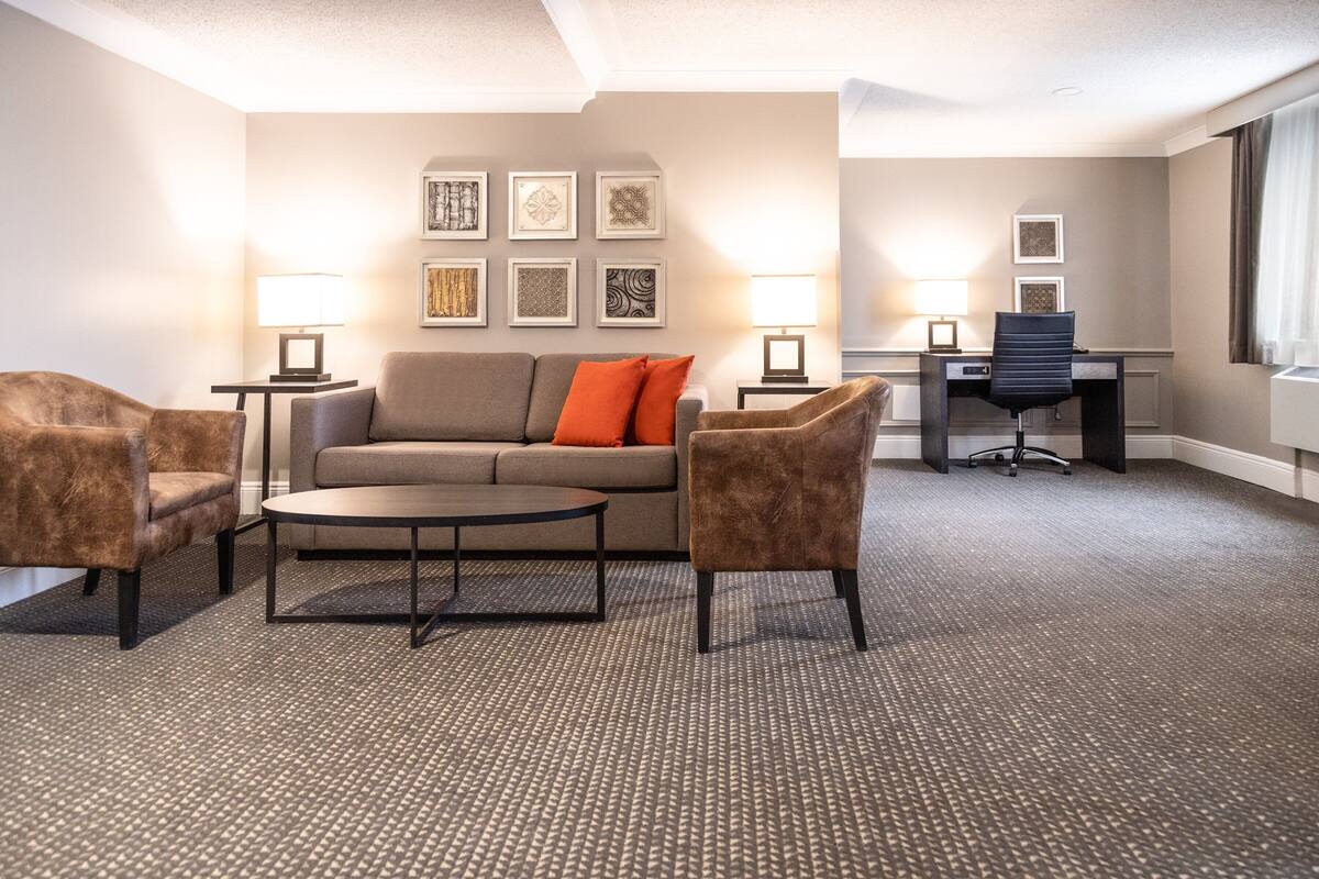 A hotel room with a sofa, two armchairs, a coffee table, a desk, and two lamps.
