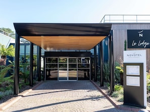 Una entrada de hotel moderna con un vestíbulo techado, puertas de vidrio y el letrero de Novotel Hotels & Resorts.