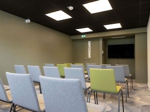 Una sala de conferencias con filas de sillas, un televisor de pantalla plana y una puerta con la leyenda 'Vancouver'.