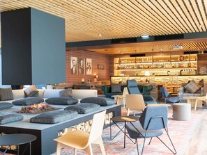 A modern lounge area with seating, a fireplace, and a bar with a variety of bottles. - Novotel Rouen Sud Zenith Parc Expo (Saint-Etienne-du-Rouvray)