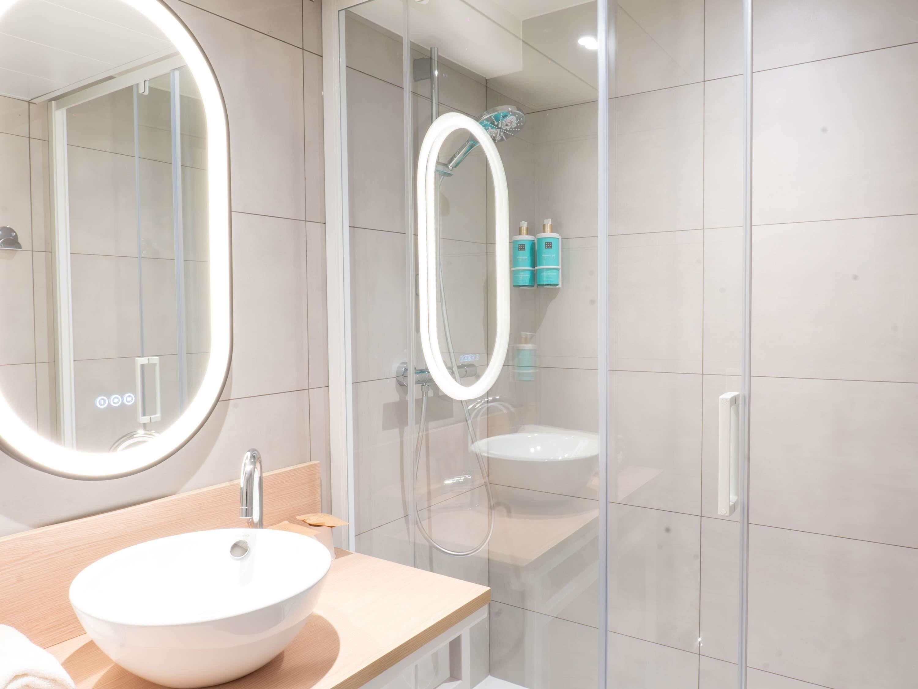Une salle de bain moderne avec un grand miroir rond, un lavabo et une douche séparée par une paroi en verre.
