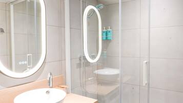 Une salle de bain moderne avec un grand miroir rond, un lavabo et une douche séparée par une paroi en verre.