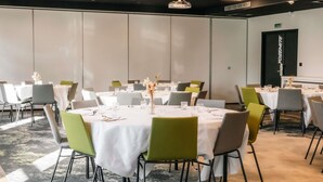 A conference room with round tables, green chairs, white tablecloths, and a carpeted floor.