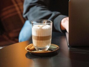 A glass of coffee on a coaster next to a laptop on a table. - Novotel Rouen Sud Zenith Parc Expo (Saint-Etienne-du-Rouvray)