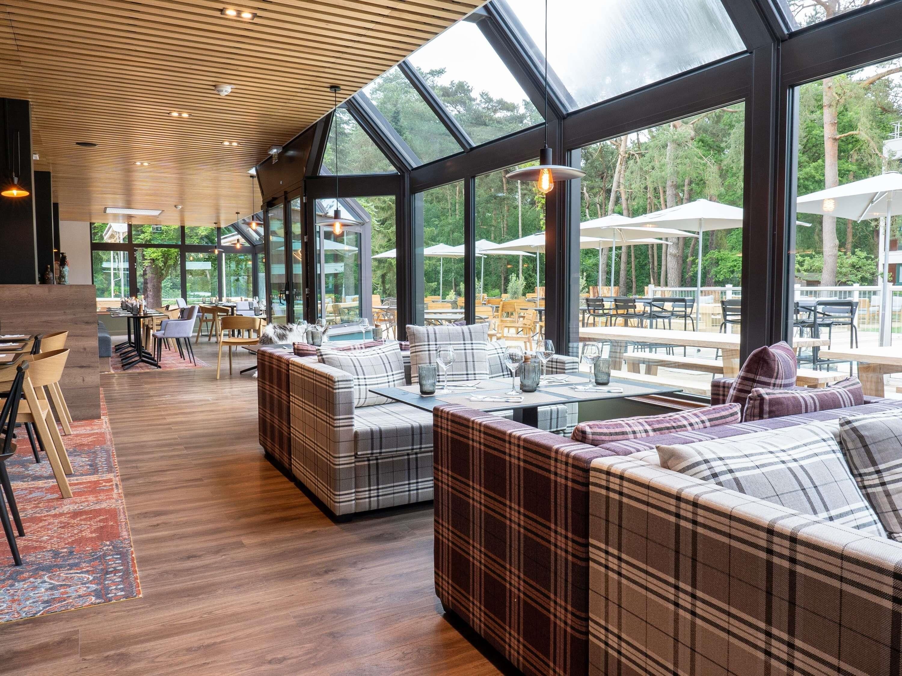A modern interior with a large glass window, wooden ceiling, and a seating area with plaid sofas.