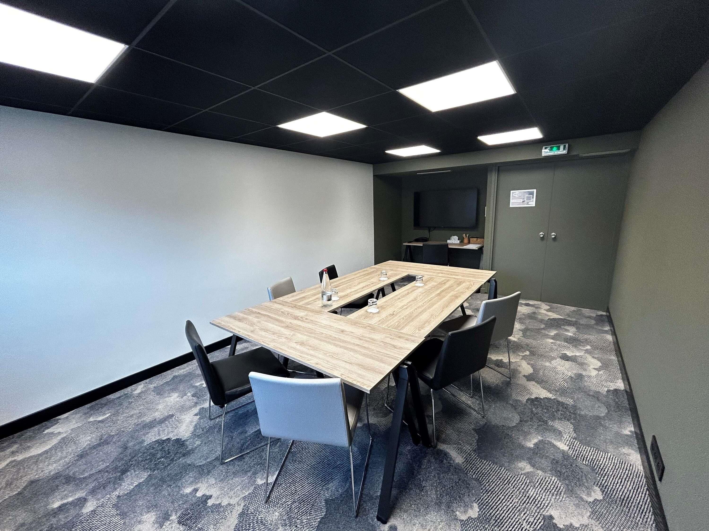 Een vergaderruimte met een lange tafel, zes stoelen, een flatscreen televisie en een vloerbedekking.