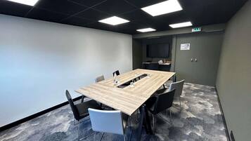 Een vergaderruimte met een lange tafel, zes stoelen, een flatscreen televisie en een vloerbedekking.