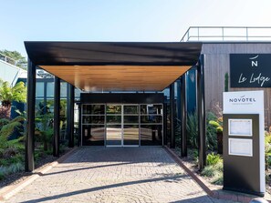 Una entrada de hotel moderna con un vestíbulo techado, puertas de vidrio y el letrero de Novotel Hotels & Resorts.