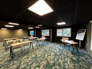 Un salón de conferencias con mesas, sillas, un proyector y una pizarra.