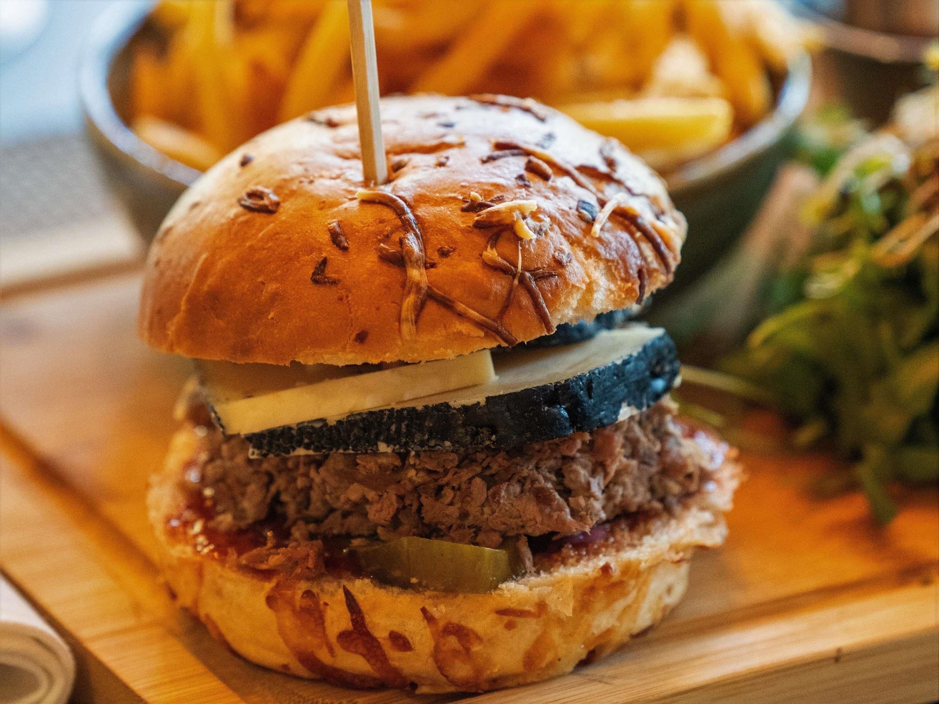 A burger with a bun, meat, cheese, and pickles.