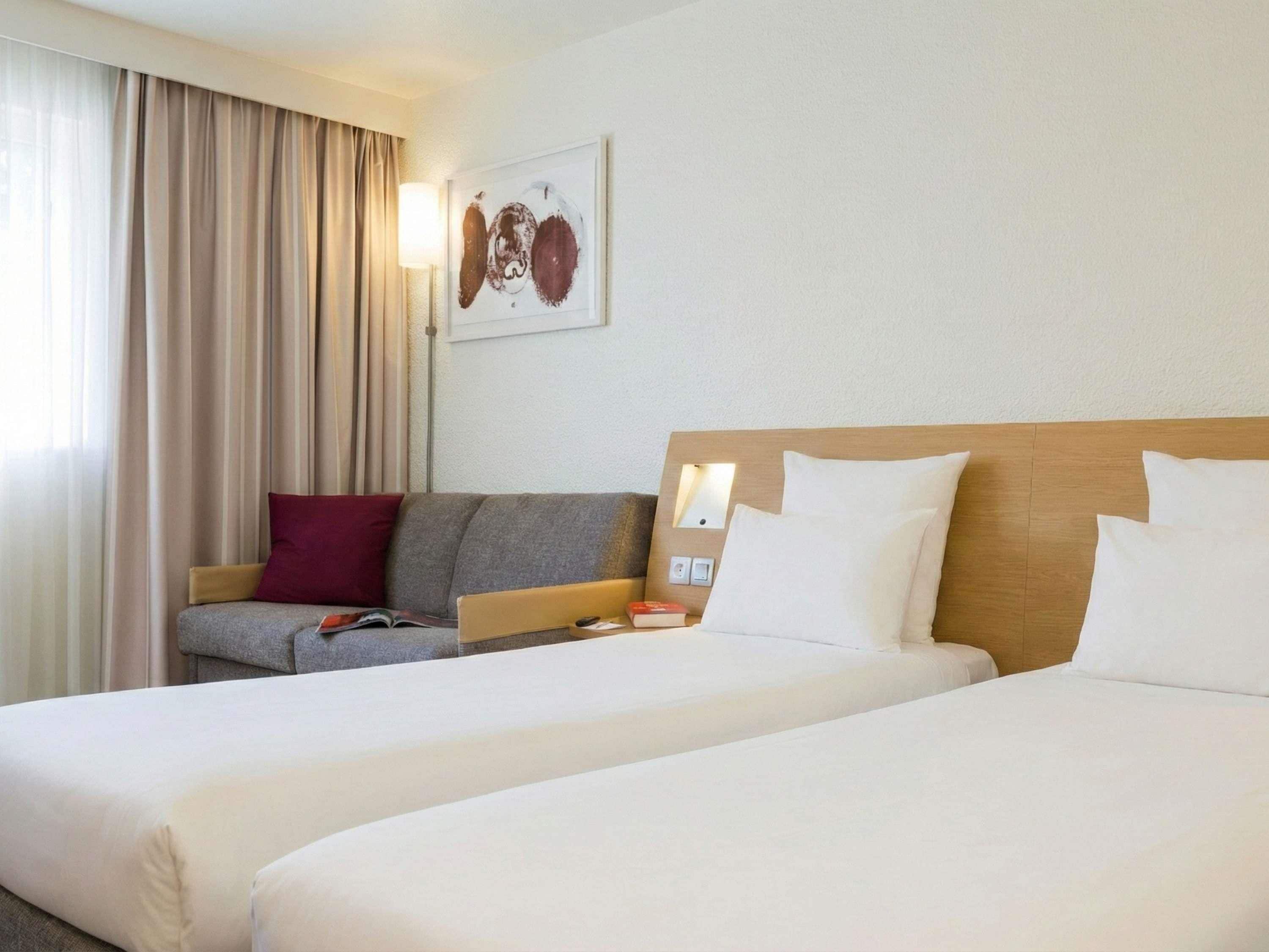 A hotel room with two beds, a sofa, a lamp, and a painting on the wall.