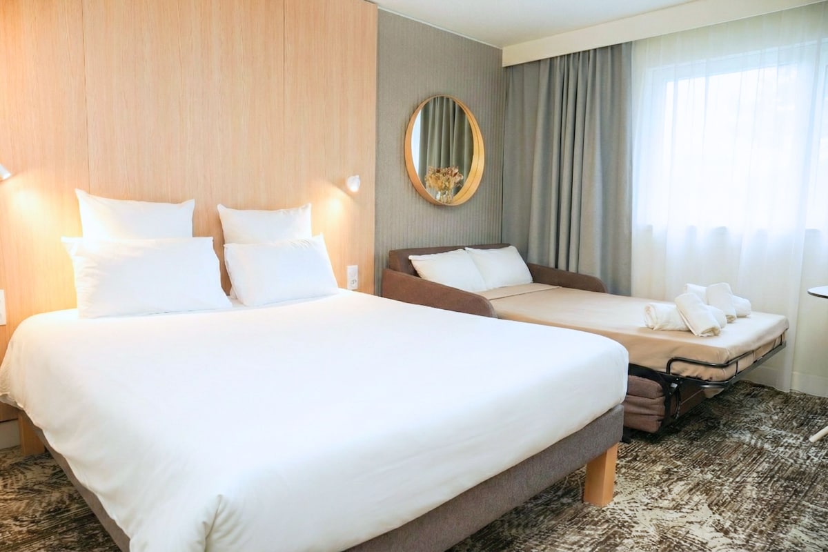 A hotel room with two beds, a large mirror, and a view of the outdoors.