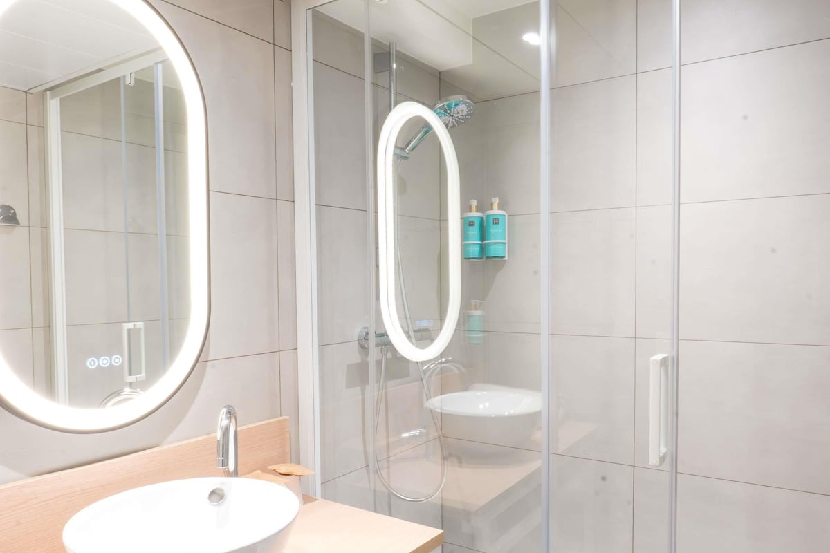 A modern bathroom with a round mirror, a sink, and a glass-enclosed shower area.