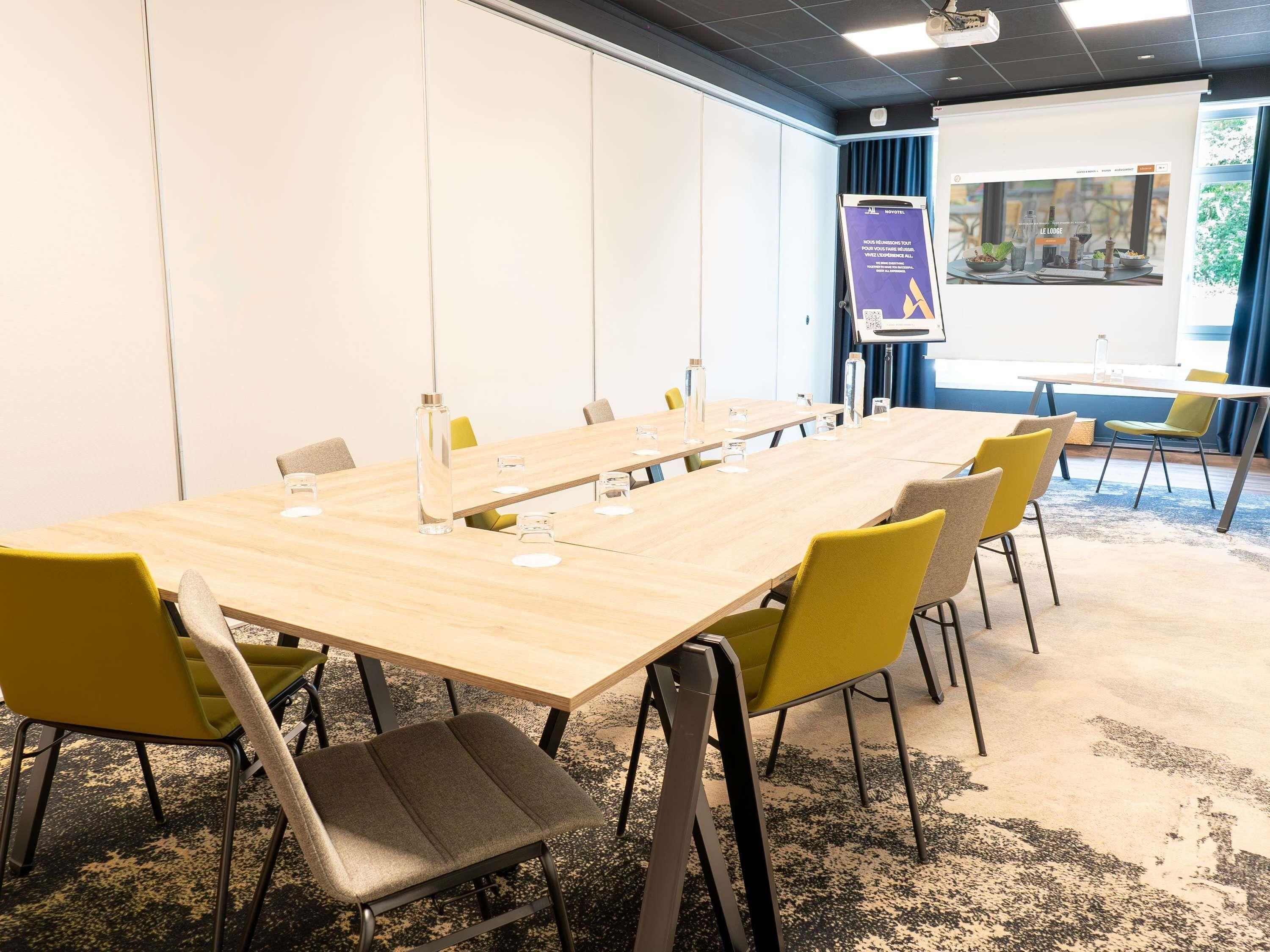 Een vergaderzaal met een lange tafel, stoelen, een projectiescherm en een presentatie aan de muur.