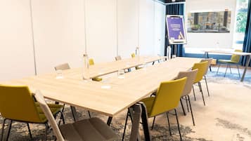 Een vergaderzaal met een lange tafel, stoelen, een projectiescherm en een presentatie aan de muur.