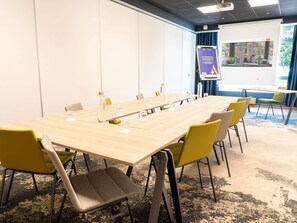 Une salle de conférence avec une longue table, des chaises, un écran de projection et une présentation affichée au mur.