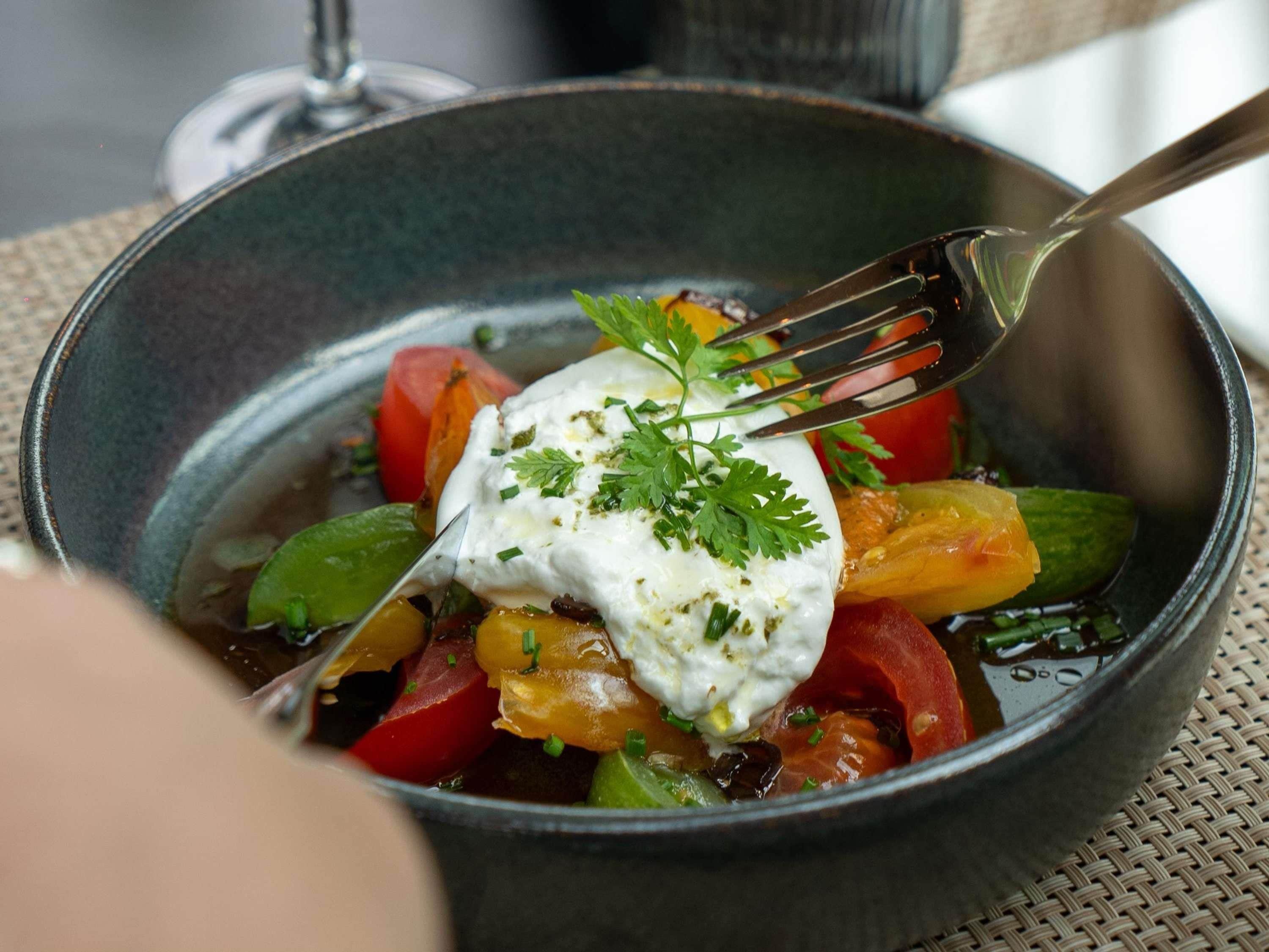 A bowl of food with a fork, containing vegetables and a dollop of sauce.