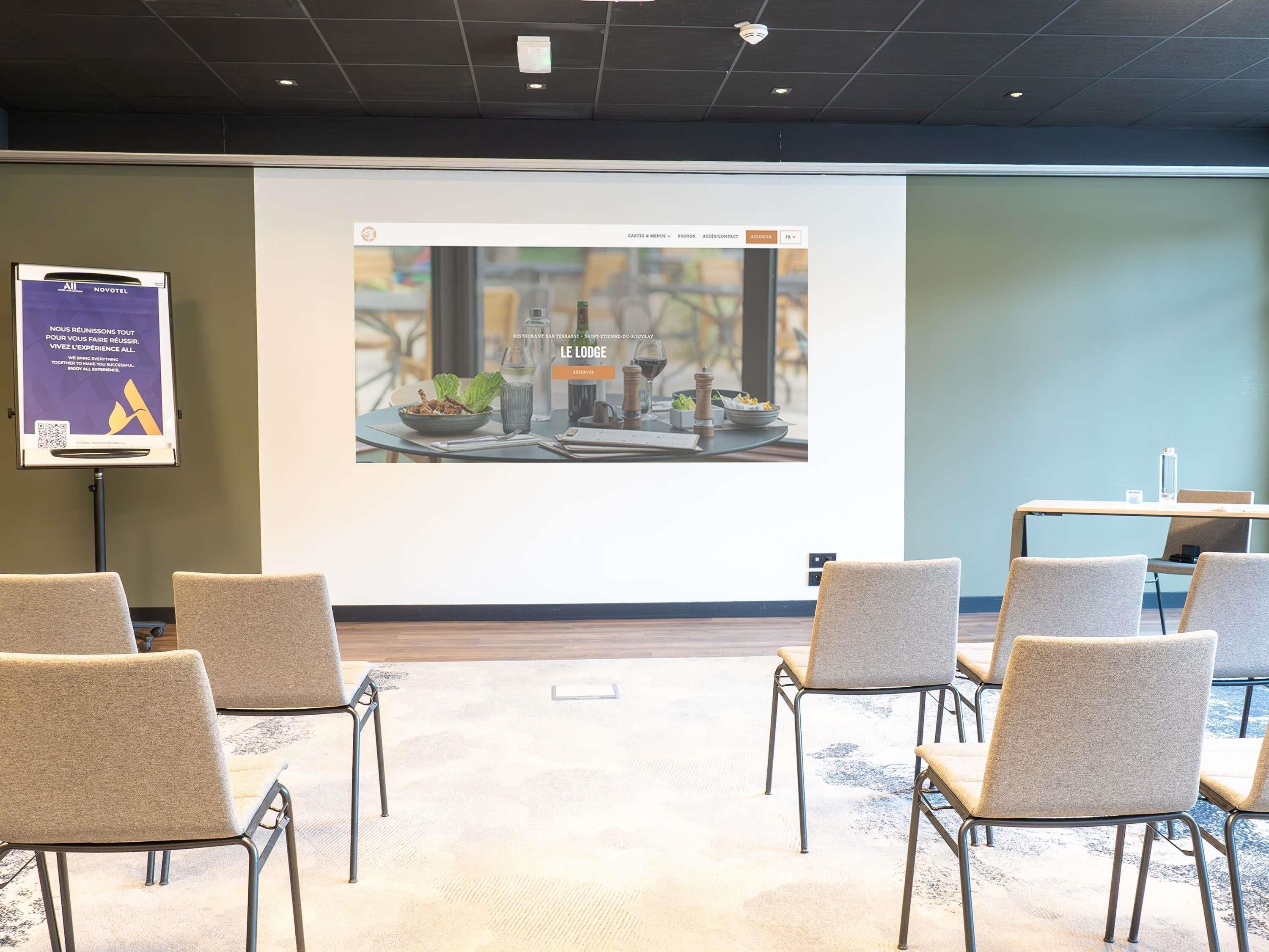 A conference room with a projection screen displaying a restaurant menu, several chairs, and a small table with a water bottle.