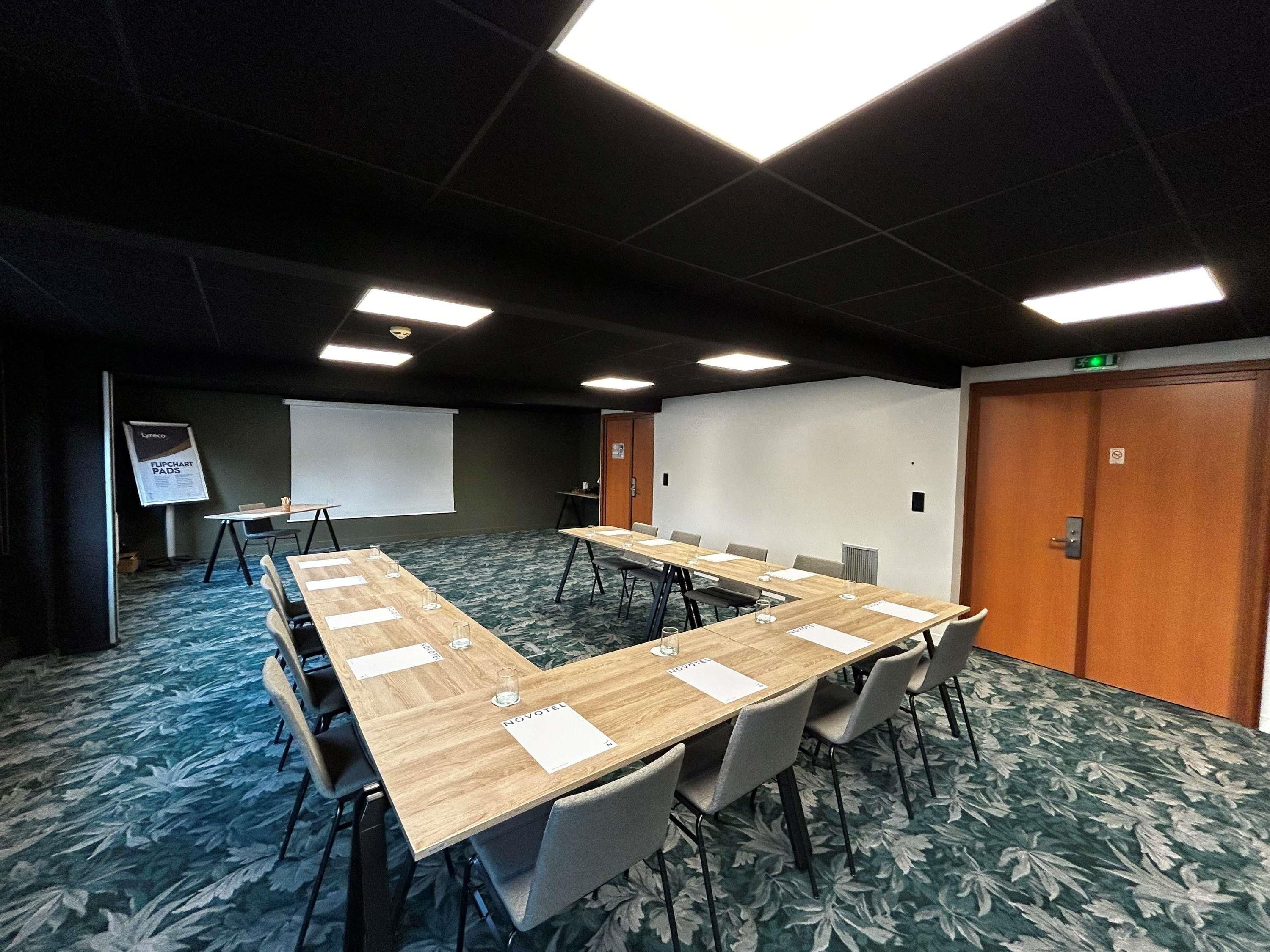 Een vergaderzaal met een lange tafel, stoelen, een scherm voor een beamer en een whiteboard.