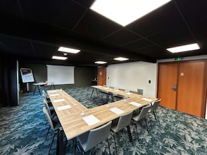 A conference room with a long table, chairs, a projector screen, and a flip chart.