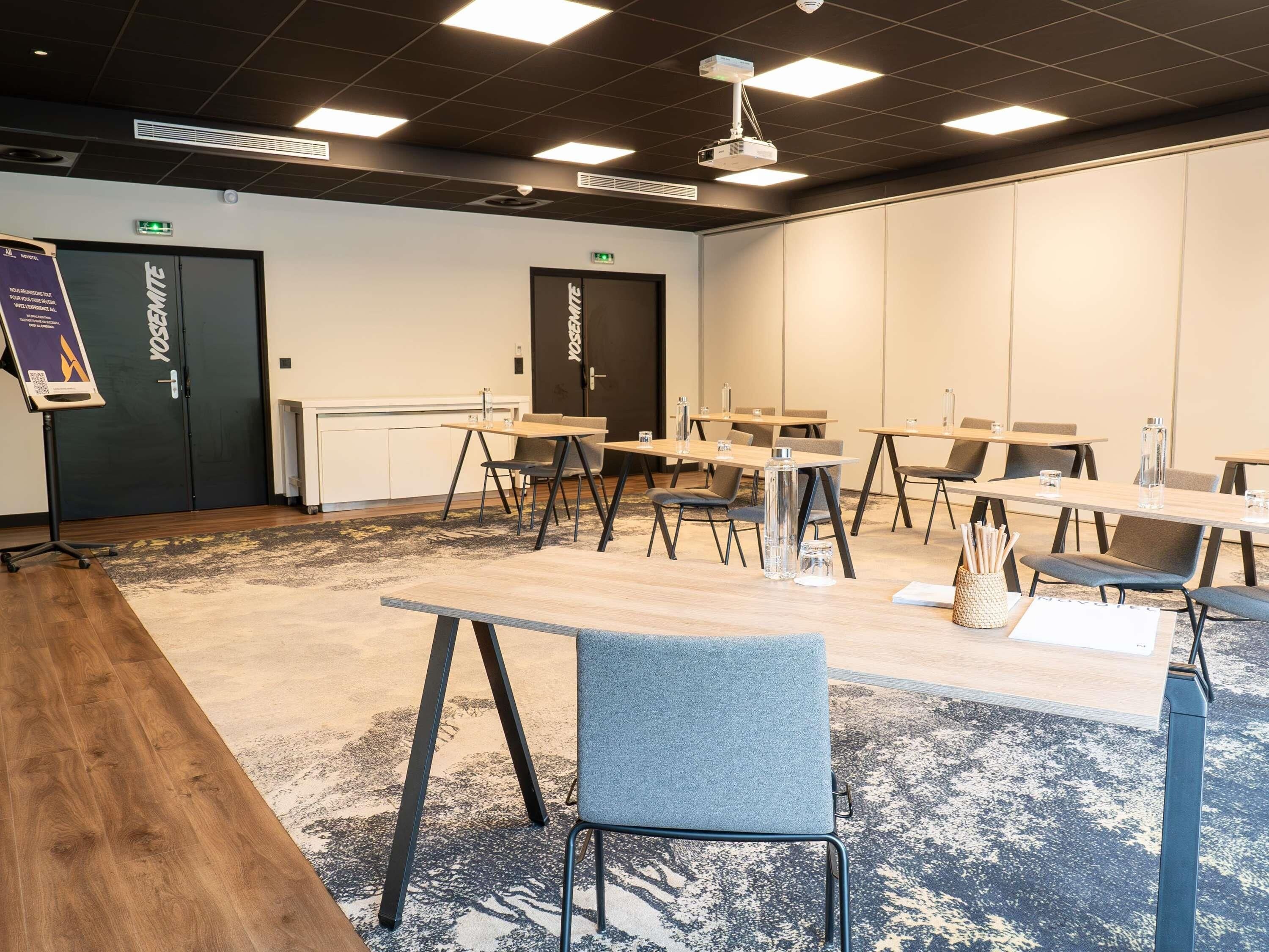 A conference room with tables, chairs, a projector, and a carpeted floor.