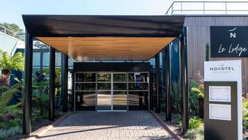 Une entrée d’hôtel moderne avec un passage couvert, des portes en verre et une enseigne indiquant « Novotel Hotels & Resorts ».