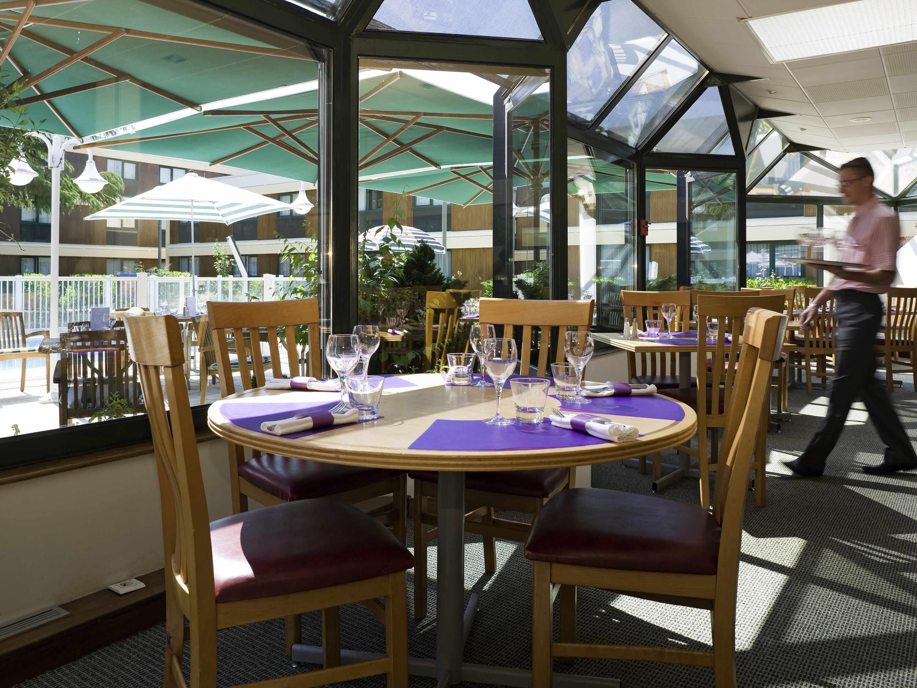Ein Restaurant mit runden Tischen, Holzsesseln und Glasveranda.