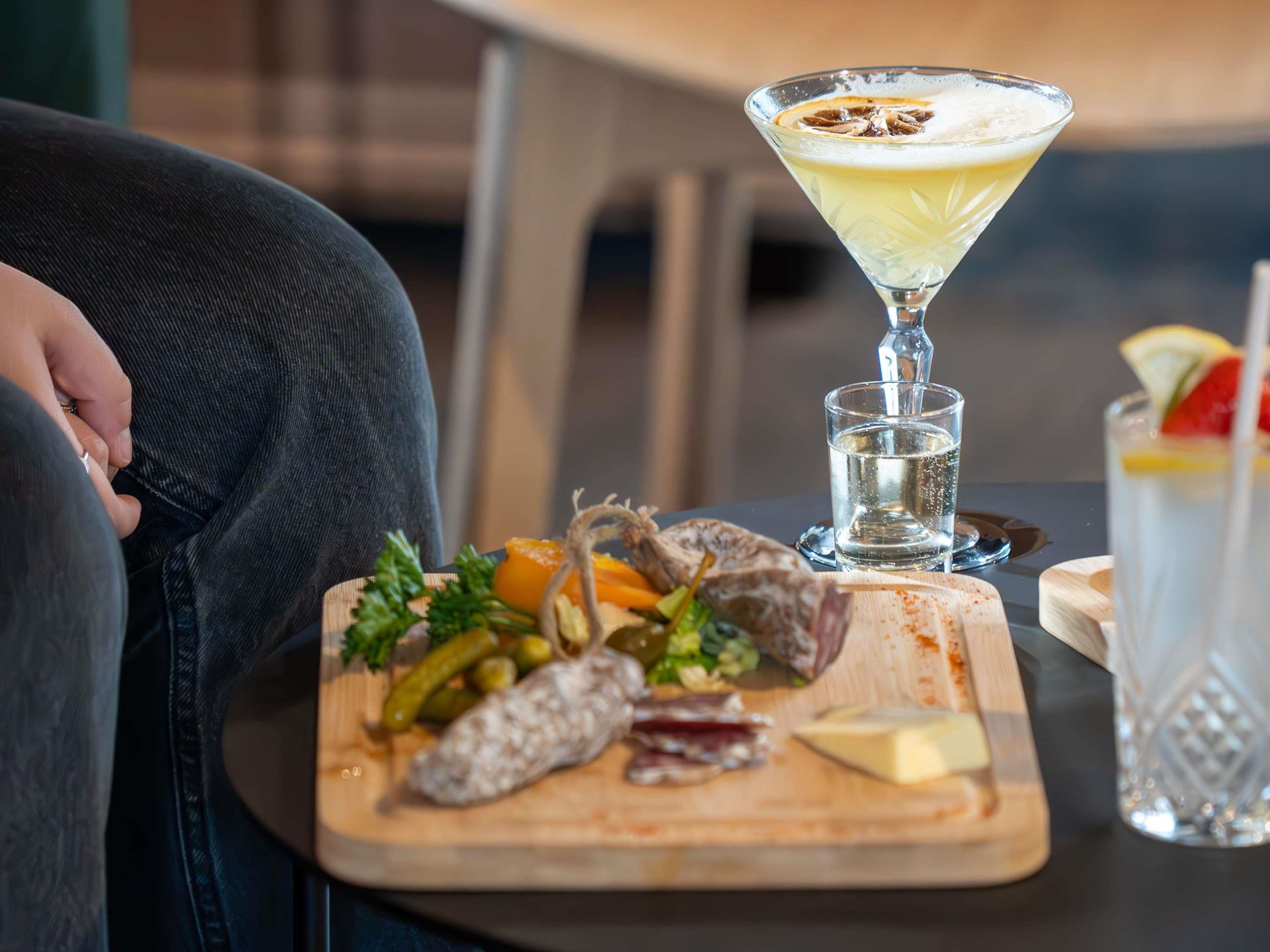 Una mesa con una tabla de embutidos, una copa de martini y un vaso de agua.
