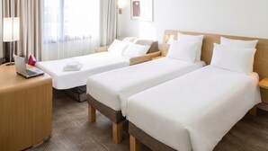 Una habitación de hotel con dos camas individuales, un escritorio con una computadora portátil y un ventanal con cortinas.