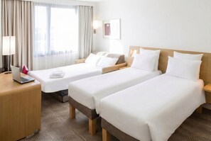 Una habitación de hotel con dos camas individuales, un escritorio con una computadora portátil y un ventanal con cortinas.