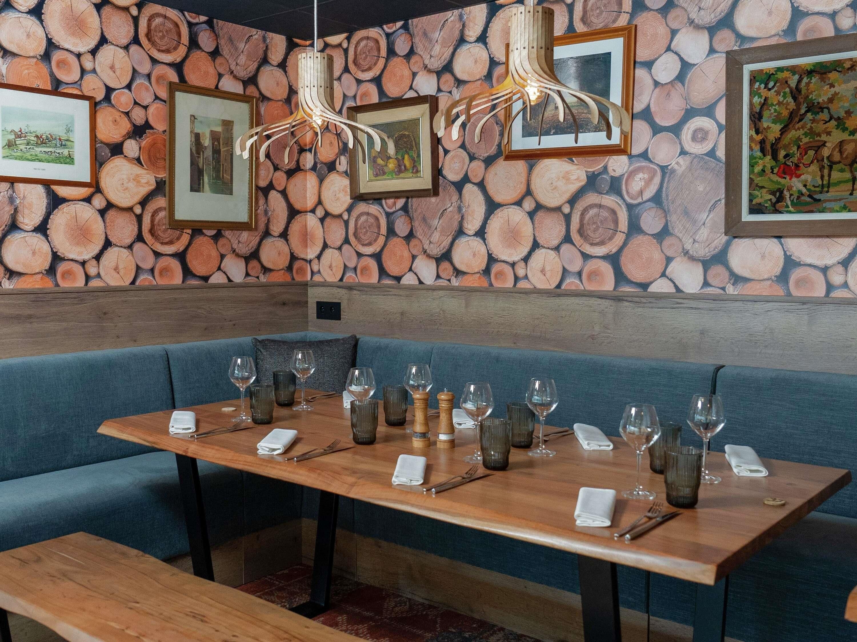 A restaurant interior with a wooden table set for dining, blue upholstered seating, and a wall adorned with a log pattern.
