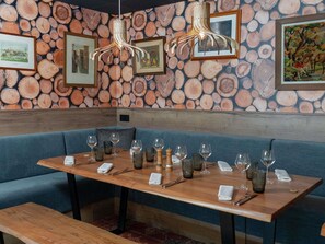 Interior de restaurante con mesa de madera dispuesta para comer, asientos tapizados en azul y pared decorada con un diseño de troncos.