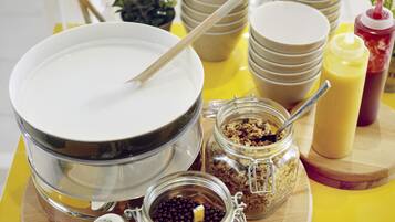 A breakfast buffet setup with bowls, jars of condiments, and a spoon.