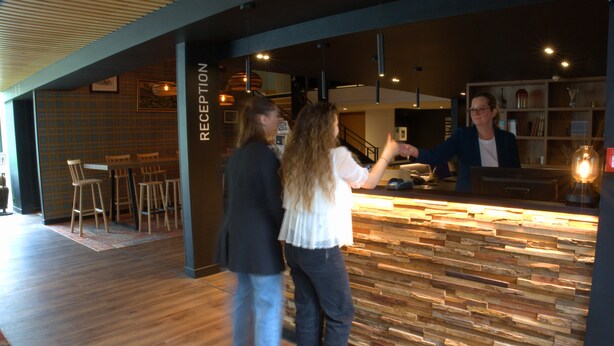 Zona de recepción con un mostrador de madera, una escalera y una zona de bar con taburetes.