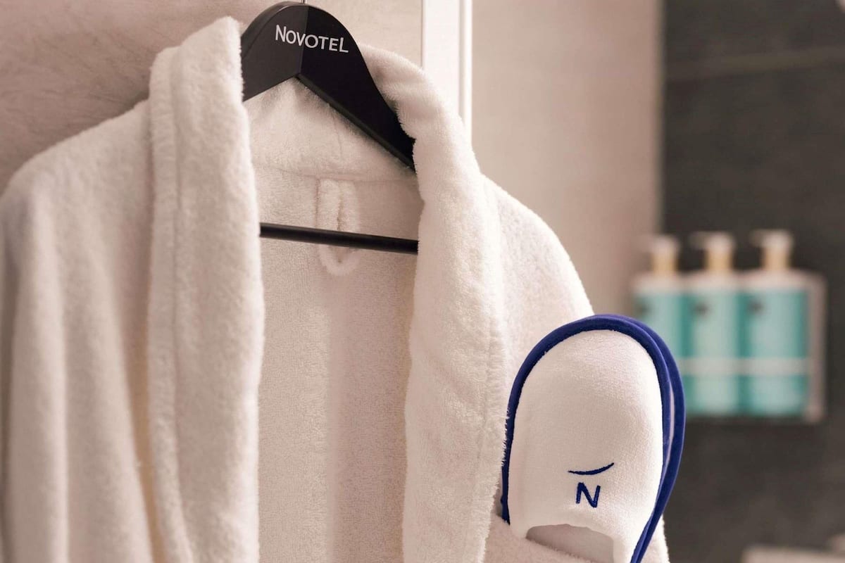 A white robe hanging on a hanger with a tag labeled "NOVOTEL" in a bathroom setting.