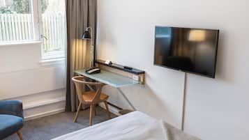 Una habitación de hotel con una cama, un escritorio con una silla, un televisor en la pared y una ventana con cortinas.
