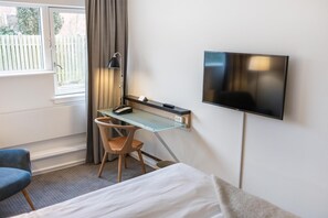 A hotel room with a bed, a desk with a chair, a TV mounted on the wall, and a window with curtains. - Gentofte Hotel (Gentofte)