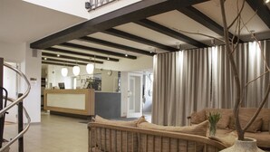 A reception area with a reception desk, a wicker sofa, a large vase, and a staircase. - Gentofte Hotel (Gentofte)