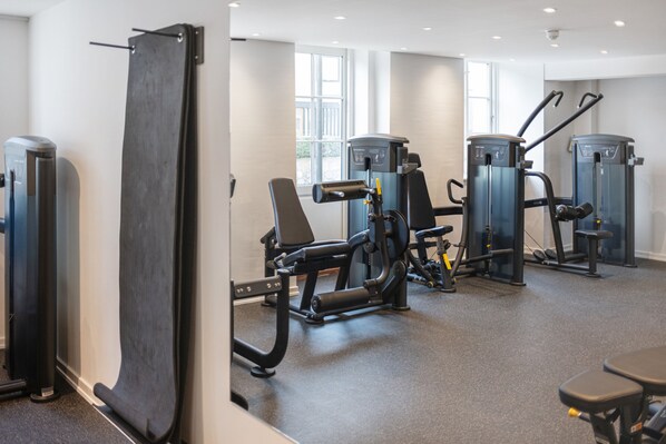 A gym with various exercise machines, a bench, and a large mirror. - Gentofte Hotel (Gentofte)