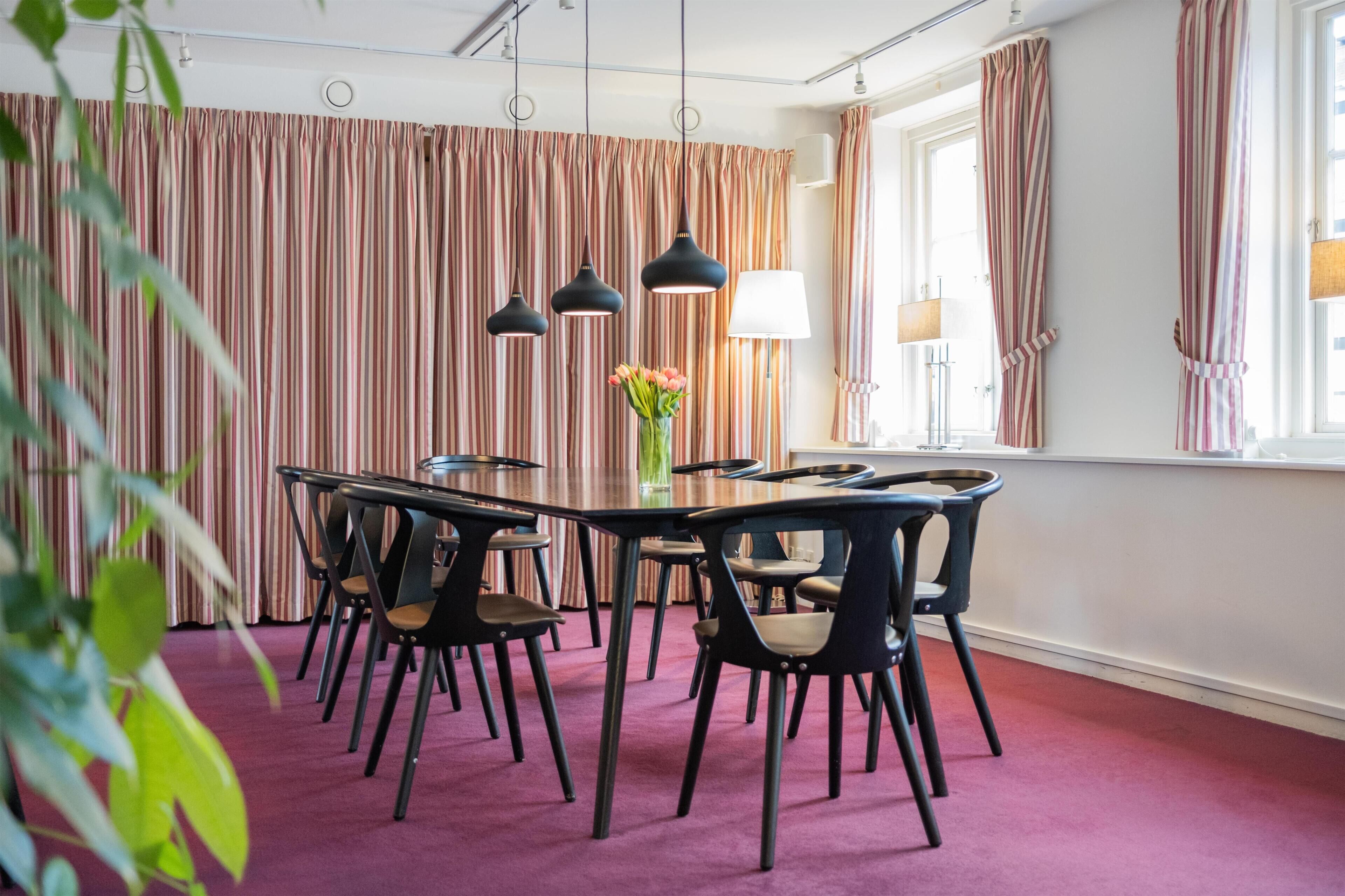 A conference room with a round table, black chairs, and a vase of flowers.