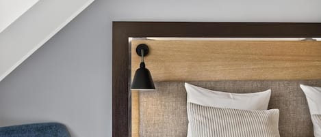 A modern bedroom with a sloped ceiling, a wooden headboard, a bedside lamp, and a blue chair.