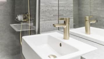 Een moderne badkamer met een wit wastafelmeubel, gouden kranen en een douchecabine van glas.