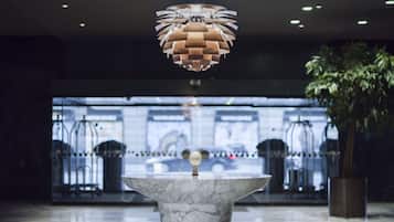 En marmorreception med et moderne pendelarmatur over, i en lobby med en glasindgang og en potteplante til højre.