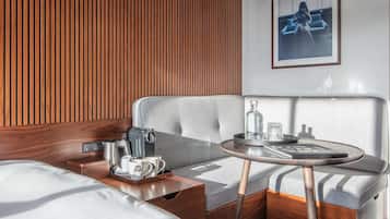 A modern hotel room with a wooden panel wall, a grey upholstered sofa, a small round table with a tray, and a coffee machine.