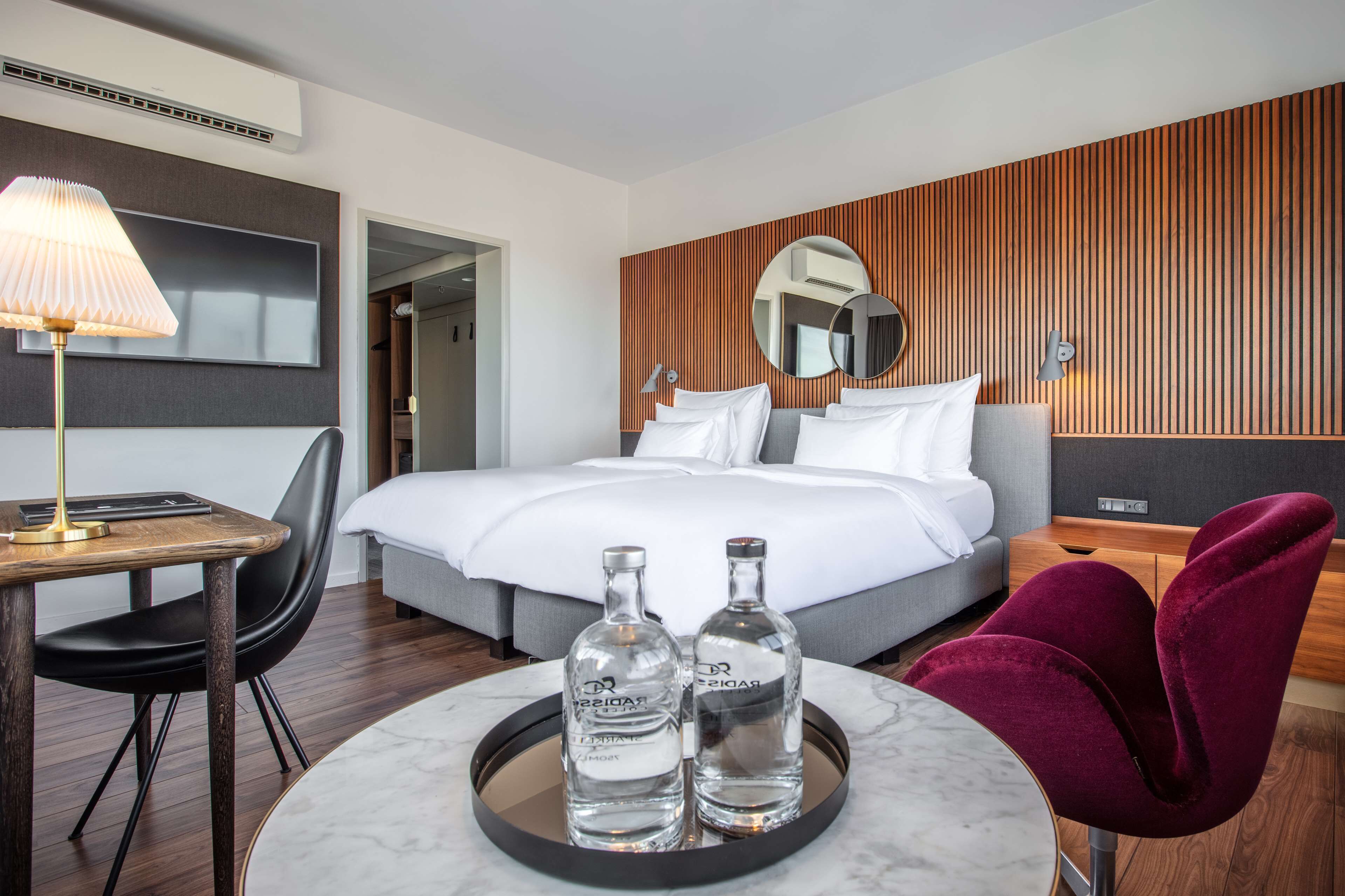 A modern hotel room with a bed, bedside table, lamp, and two bottles of water on a tray.