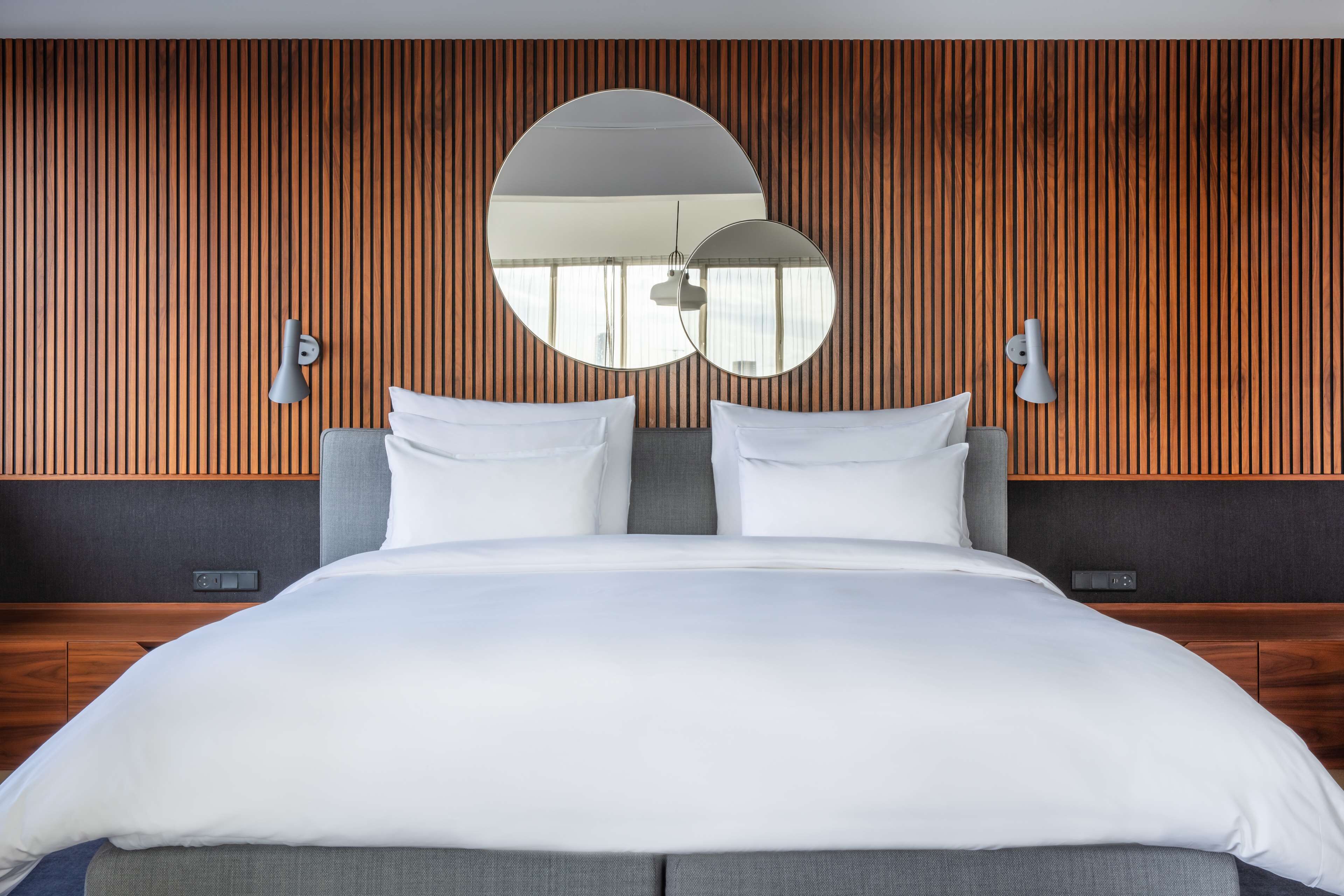 Un dormitorio moderno con una cama grande, dos lámparas de pared y un espejo amplio.