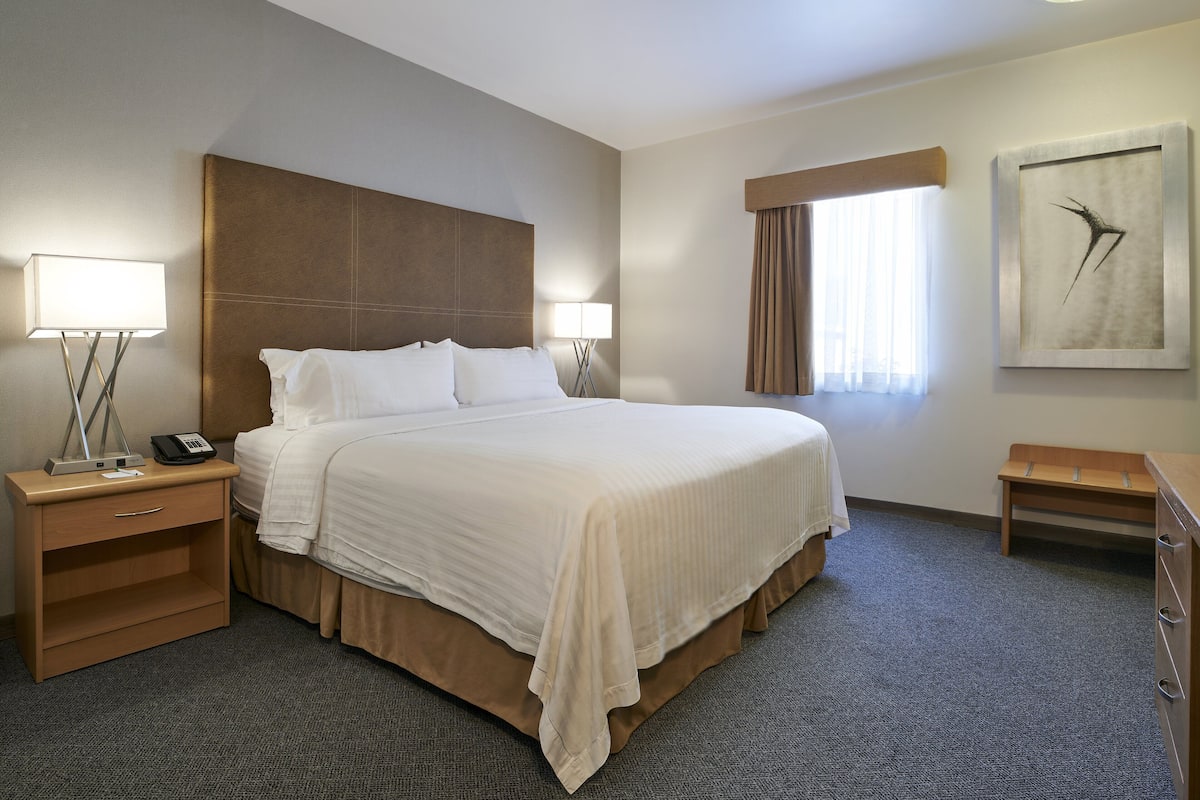 A hotel room with a large bed, bedside tables, a lamp, a telephone, a small wooden side table, and a framed picture on the wall.