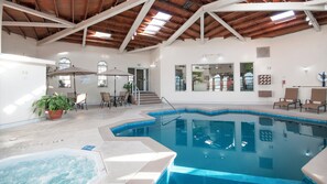 An indoor swimming pool with a hot tub, surrounded by lounge chairs and a dining area.