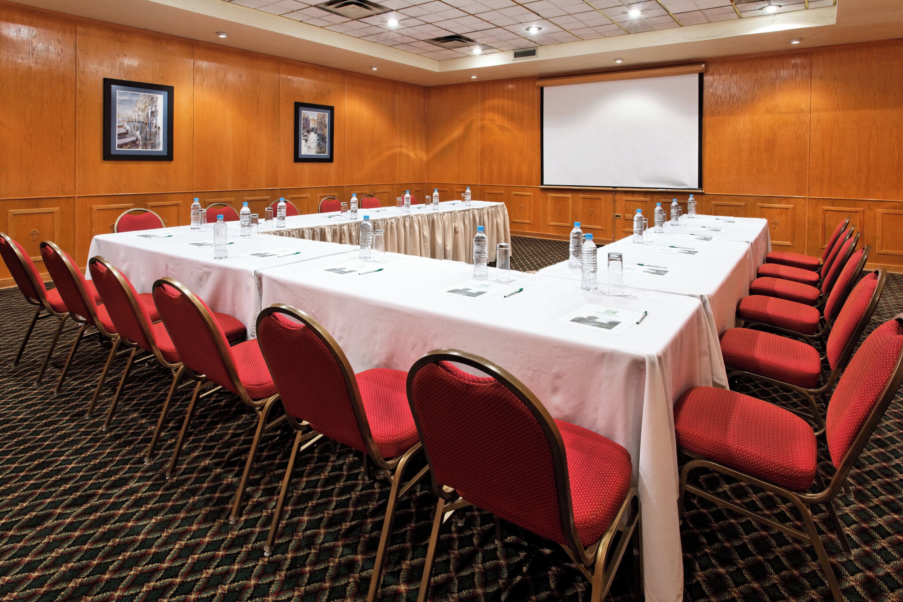 A conference room with a long table, red chairs, and a projector screen.