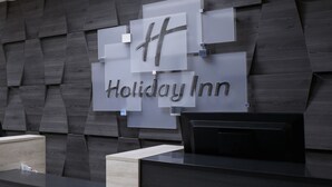 Un comptoir d’accueil de l’hôtel Holiday Inn, doté d’un design moderne, avec un mur en panneaux de bois foncé et un élégant comptoir noir.